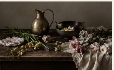 Floral stems, a brass pitcher, and tools arranged on a worktable